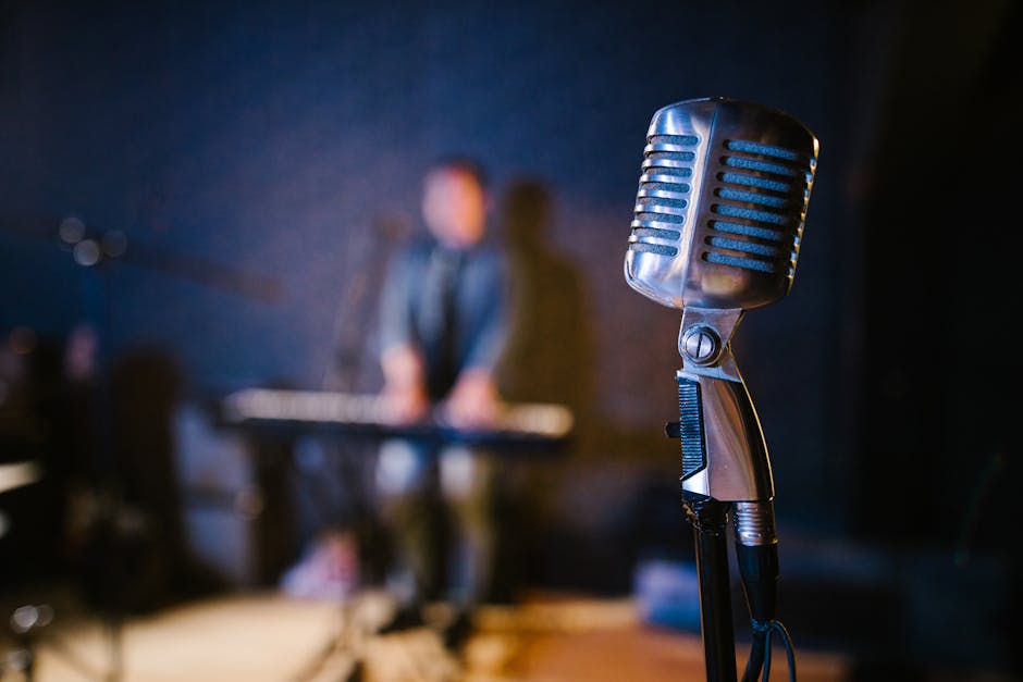 Close-up of a vintage microphone with a musician playing keyboard in the background, creating a musical atmosphere.