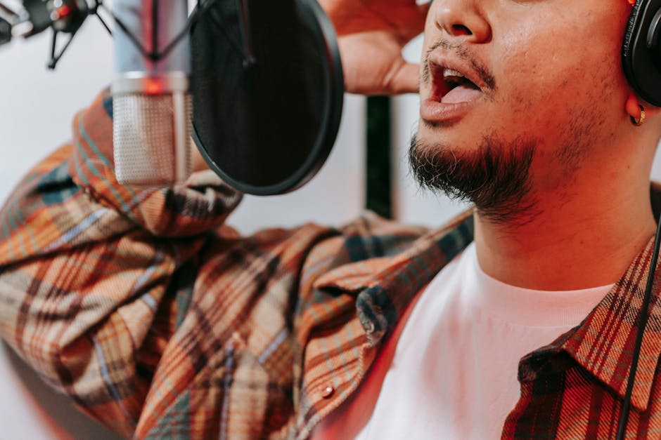 A male singer recording vocals with a condenser microphone and pop filter in a studio.