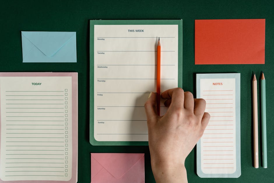 Flat lay of stationery items including planners, envelopes, and pencils on a green surface.